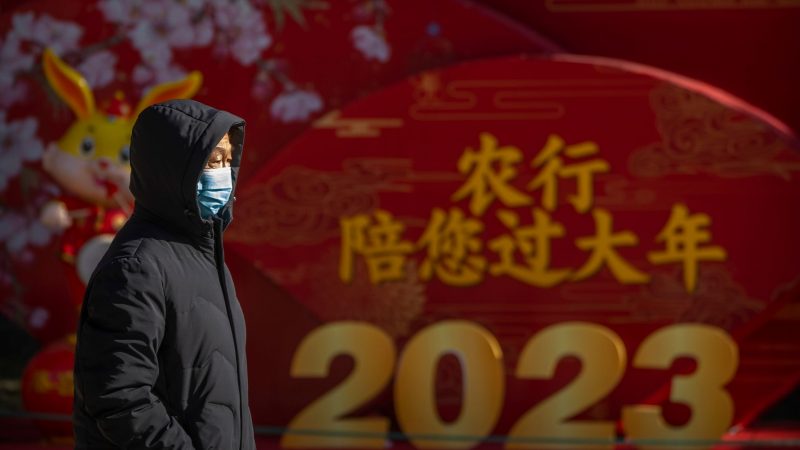 Ein Mann mit Mund-Nasen-Schutz läuft in einem öffentlichen Park in Peking an einem Plakat für zum Mondneujahr vorbei.