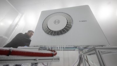 Ein Mitarbeiter der Bosch Thermotechnik GmbH öffnet in einer Klimakammer das Gehäuse einer Bosch-Wärmepumpe.