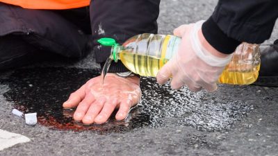 Polizisten in Hannover versuchen festgeklebte Hände von Aktivisten der Gruppierung «Letzte Generation» mit Speiseöl von der Straße zu befreien.
