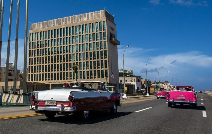 Touristen fahren auf dem kubanischen Malecon in klassischen Cabriolets an der US-Botschaft vorbei.