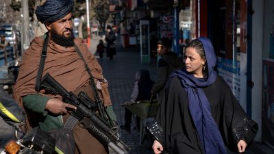 Eine Frau läuft in Kabul an einem bewaffneten Taliban-Kämpfer vorbei. Laut Amnesty International verschlechtert sich die Menschenrechtslage in Afghanistan rapide.