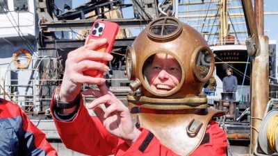 Ein Besucher macht zur Saisoneröffnung im Deutschen Hafenmuseum in Hamburg – Standort Schuppen 50A, ein Selfie, nachdem er sich einen historischen Taucherhelm aufgesetzt hat.
