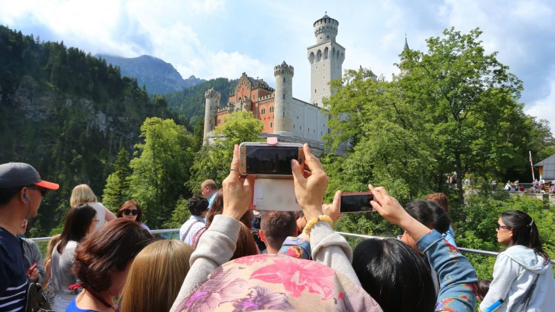 Touristen stehen auf einer Aussichtsplattform unterhalb des Schlosses Neuschwanstein.