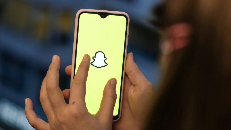 Ein Mädchen hält ihr Smartphone in den Händen, auf dem das Logo von Snapchat zu sehen ist.