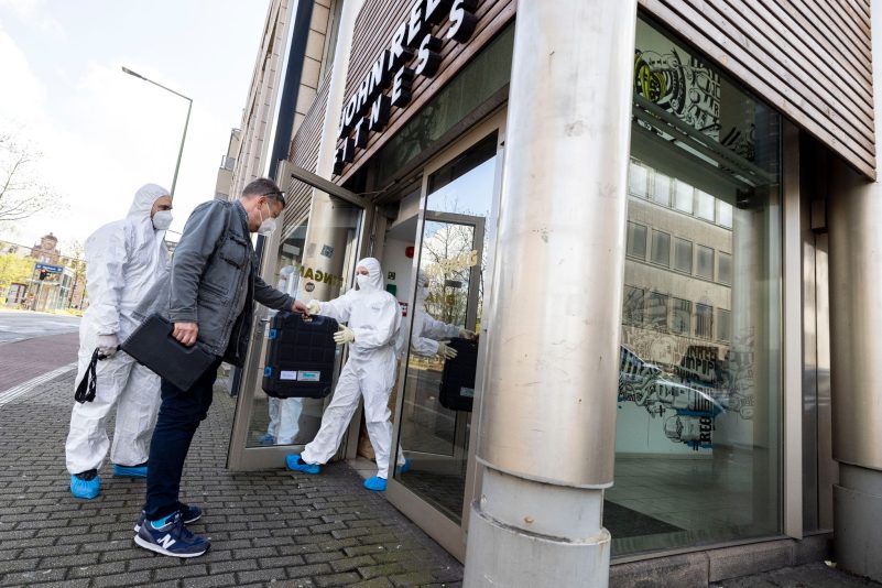 Ein Beamter in zivil bringt den vor Ort anwesenden Beamten der Spurensicherung technisches Equipment zum Tatort.