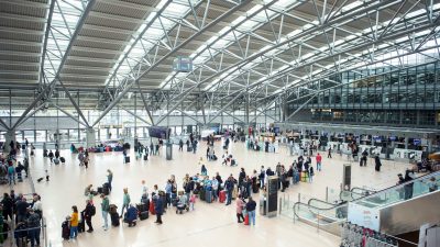 Reisende stehen im Terminal des Flughafen Hamburg mit ihrem Gepäck in einer Warteschlange an einem Check in-Schalter.
