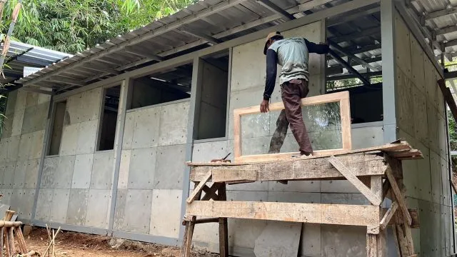 Ein Mann arbeitet am Rohbau eines einfachen Hauses, bei dem gebrauchte Windeln einen Teil des Baumaterials ersetzen.