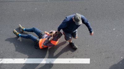 Ein Verkehrsteilnehmer (r) zieht bei einer Blockade der Letzten Generation auf der Autobahn 100 eine Aktivistin von der Straße. Erneut hat die Klimaaktivistengruppe an zahlreichen Stellen in der Stadt Straßen blockiert.