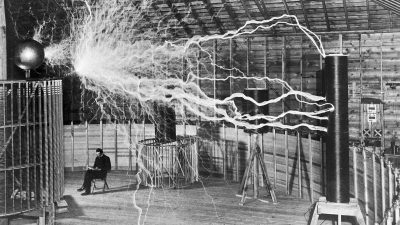 Nikola Tesla in seinem Labor in Colorado Springs (USA, Dezember 1899). Die Aufnahme ist eine Mehrfachbelichtung, während der Blitzentladungen befand sich Tesla nicht im Raum.