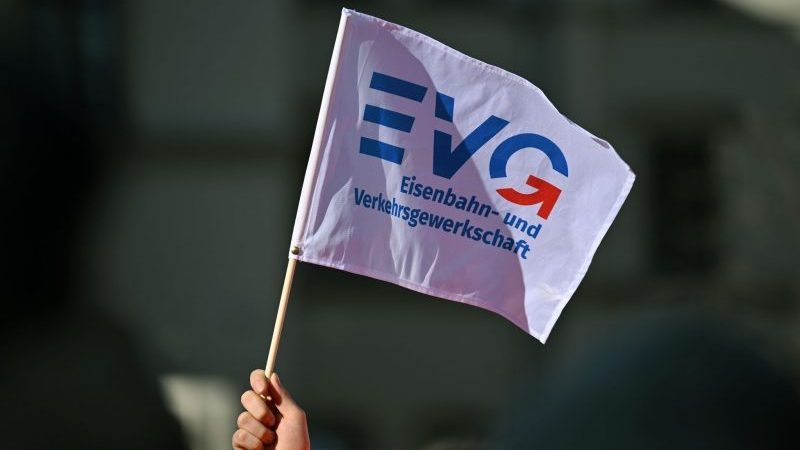 Ein Teilnehmer am Warnstreik Ende März vor dem Erfurter Hauptbahnhof mit einem Fähnchen der Eisenbahn- und Verkehrsgewerkschaft (EVG).