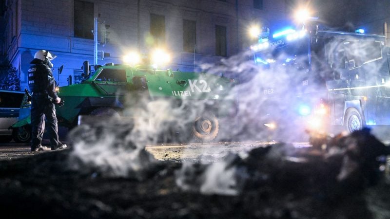 Polizisten stehen hinter einer rauchenden Barrikade im Stadtteil Connewitz in Leipzig.