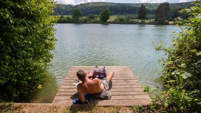 Ein Mann genießt die Sonne am Badesee Plüderhausen - und vielleicht auch den ein oder anderen Sommerhit.