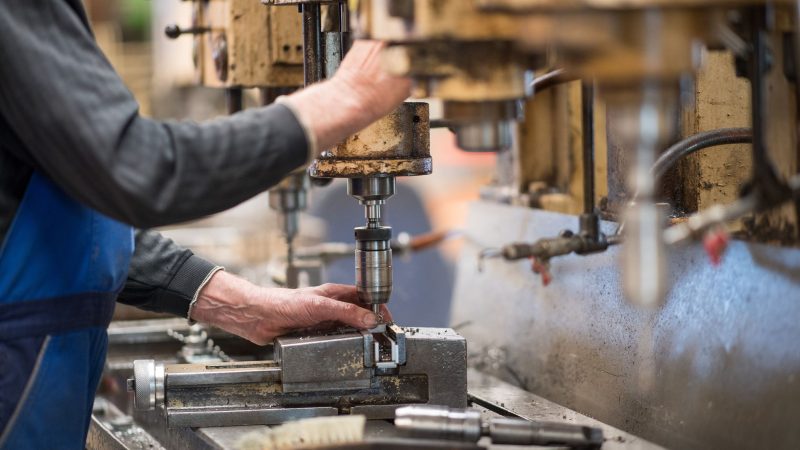 Ein Mitarbeiter bedient in der Produktionshalle eine Maschine zur Verarbeitung von Metall.