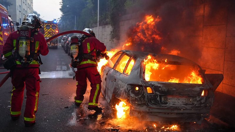 Feuerwehrleute löschen am Rande von Ausschreitungen westlich von Paris ein brennendes Auto.