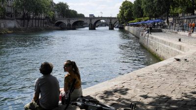 Zwei junge Leute sitzen am Ufer der Seine in Paris.