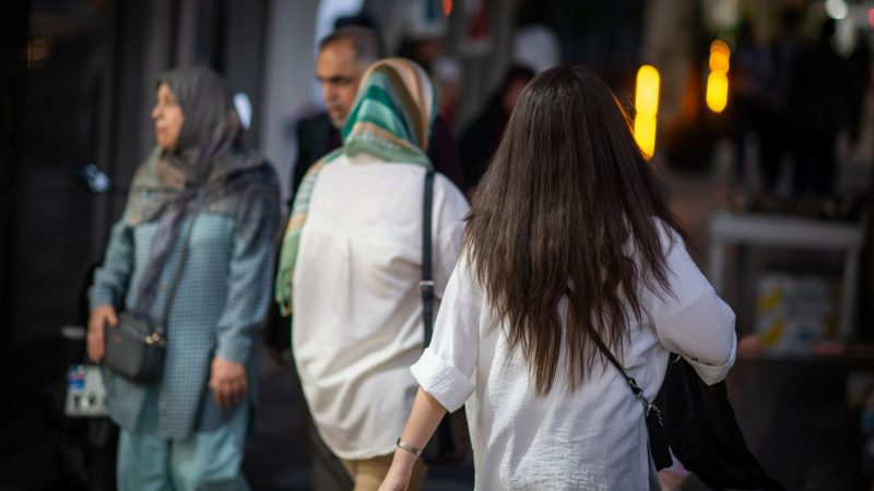 Eine Frau läuft in Teheran mit offenen Haaren eine Straße entlang. Das ist im Iran eigentlich verboten.