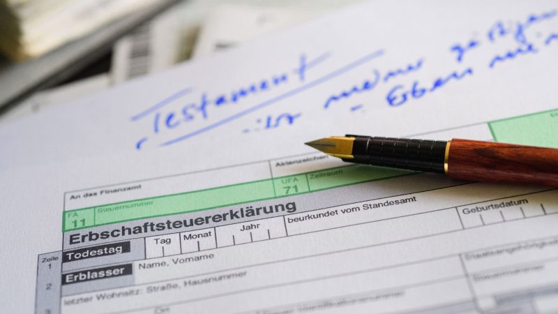 Ein Formular für die Erbschaftsteuererklärung sowie Stift und Testament liegen auf einem Tisch. (Symbolbild)