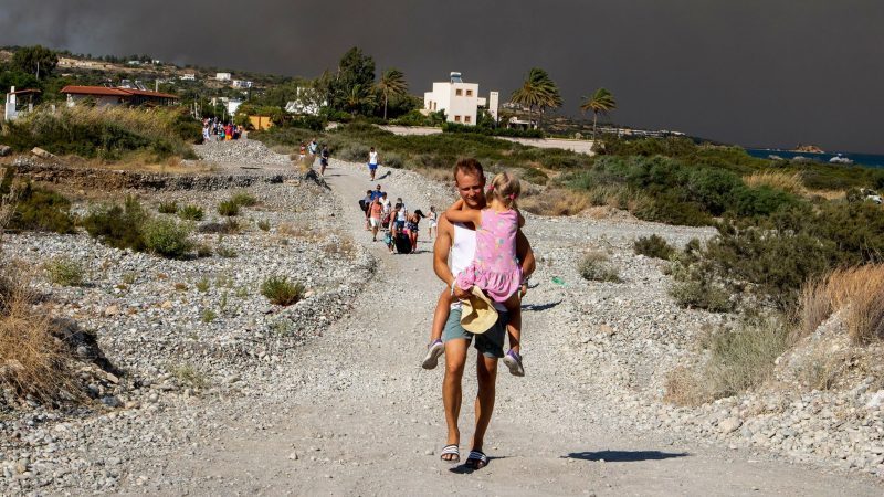 Zu Fuß verlassen Menschen ein Waldbrandgebiet auf Rhodos. Wegen der schweren Waldbrände auf der griechischen Ferieninsel sind seit Samstag 19.000 Menschen aus Dörfern und Hotels in Sicherheit gebracht worden.
