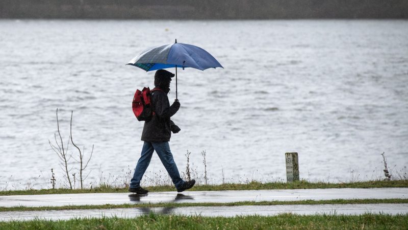 Spaziergänger mit Regenschirm am Ufer des Kemnader Sees in Bochum.