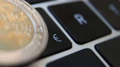 Eine Zwei-Euro-Münze liegt auf der Tastatur eines Laptops neben einem Eurozeichen.