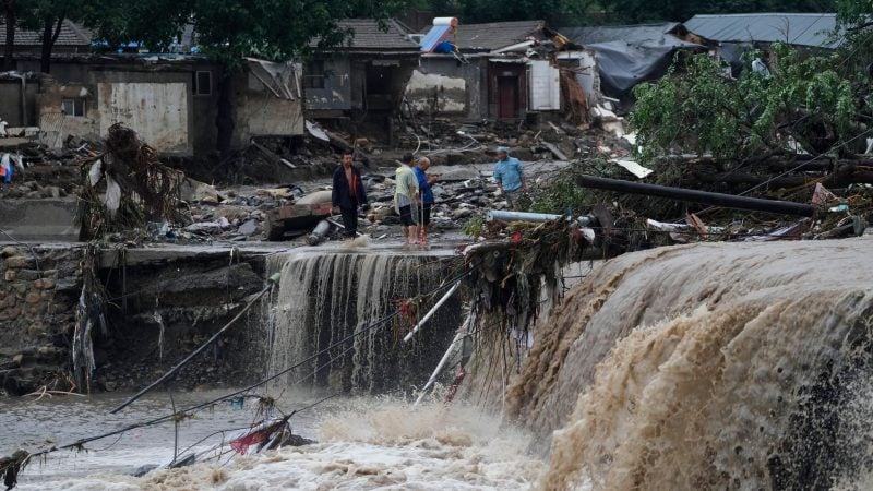 Menschen stehen in Peking vor von den Wassermengen zerstörten Häusern. Die extremen Regenfälle sind eine Folge des Tropensturms «Doksuri».
