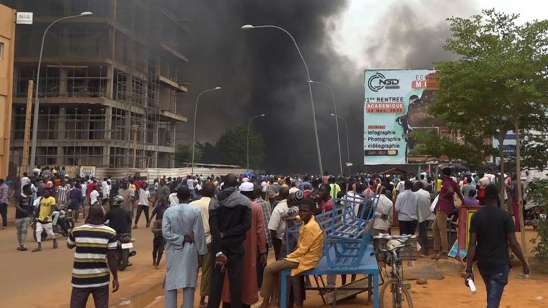 Vor der Kulisse des brennenden Hauptquartiers der Regierungspartei demonstrieren Anhänger meuternder Soldaten in Niamey.