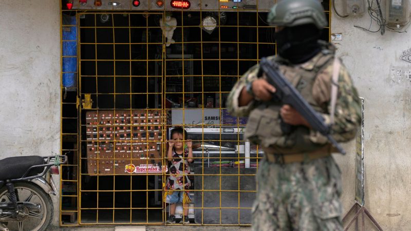 Ein Junge schaut hinter den Gitterstäben eines geöffneten Elektronikgeschäfts hervor, während ein Soldat an einem von der Armee eingerichteten Sicherheitskontrollpunkt Wache steht.