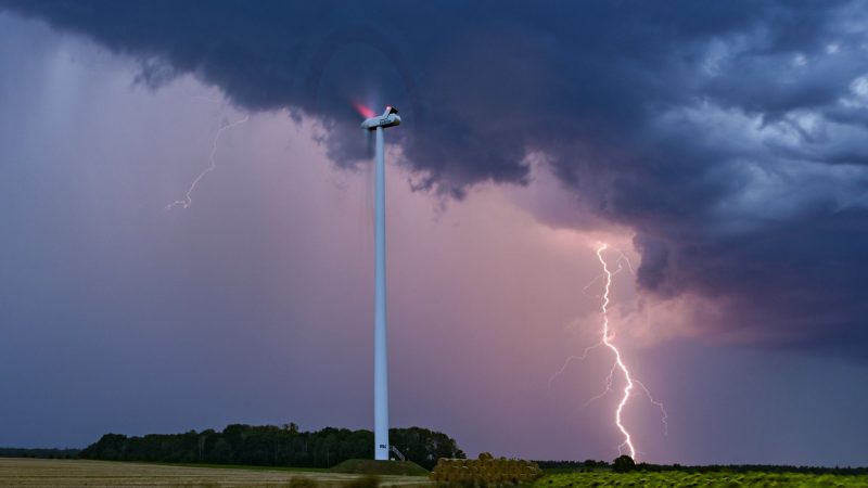 Ein Blitz leuchtet am Abendhimmel hinter einer Windenergieanlage im Osten Brandenburgs.