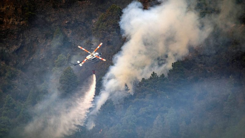 Ein Hubschrauber wirft Wasser auf die Flammen, während sich das Feuer durch den Wald in Richtung der Stadt Pinolere ausbreitet.