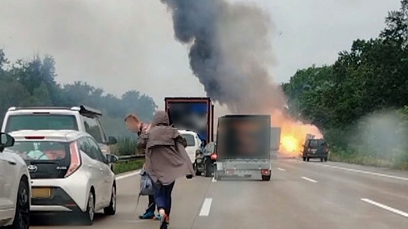 Autofahrer verlassen ihre Fahrzeuge, während im Hintergrund ein Lkw in Flammen steht. Nach einem Auffahrunfall sind auf einem Gefahrguttransporter mehrere Gasflaschen explodiert.