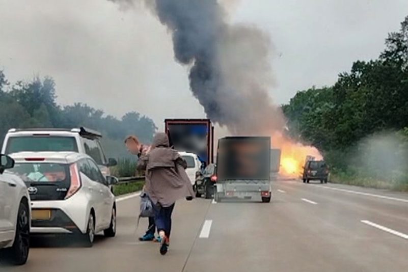 Autofahrer verlassen ihre Fahrzeuge, während im Hintergrund ein Lkw in Flammen steht. Nach einem Auffahrunfall sind auf einem Gefahrguttransporter mehrere Gasflaschen explodiert.