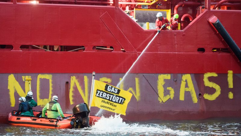 Greenpeace-Aktivisten liegen mit einem Schlauchboot vor einem Schiff im Hafen von Mukran.