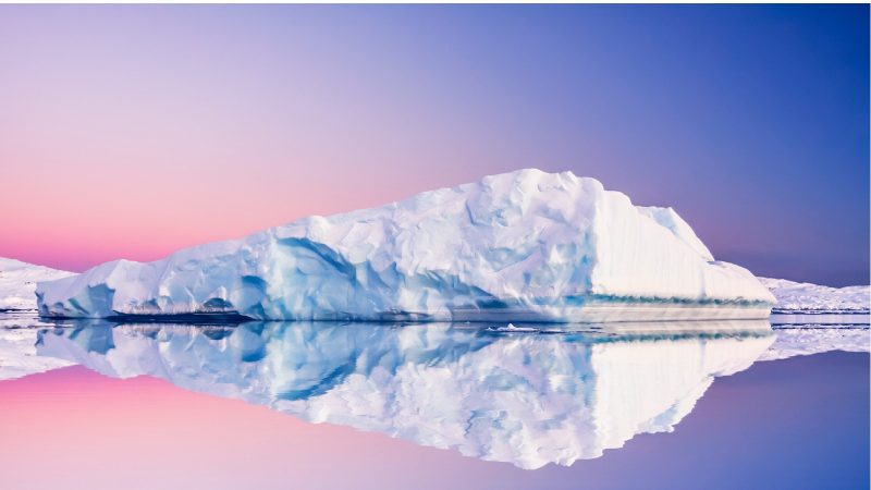 Sonnenuntergang in der Antarktis: Ein Eisberg spiegelt sich im Wasser.