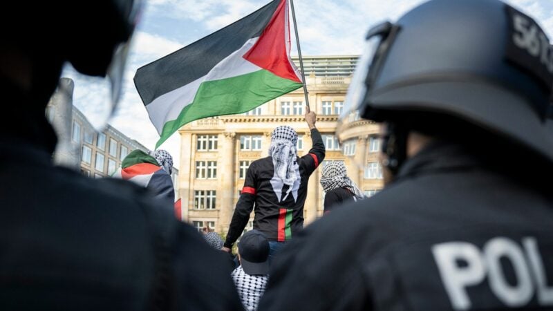 Ein Teilnehmer einer verbotenen Pro-Palästina-Demonstration in Frankfurt am Main schwenkt eine Palästina-Flagge, während Polizisten die Situation beobachten.