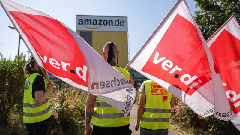 Streikende stehen mit Fahnen von Verdi vor einem Verteilzentrum des Online-Händlers Amazon in Leipzig. (Archivbild)