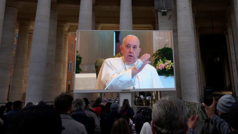 Papst Franziskus ist auf einem Monitor zu sehen, um die Gläubigen zu segnen, die sich auf dem Petersplatz versammelt haben.