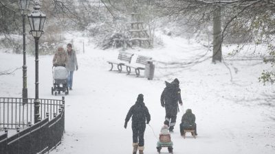 Menschen spazieren durch den verschneiten Volkspark Friedrichshain in Berlin.
