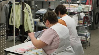 Zwei Frauen arbeiten in der Wäscherei der Lebenshilfe Gera e.V und legen dort Wäsche zusammen.