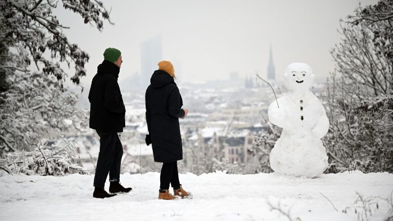 Zwei Spaziergänger wandern am Fockeberg an einem Schneemann vorbei.