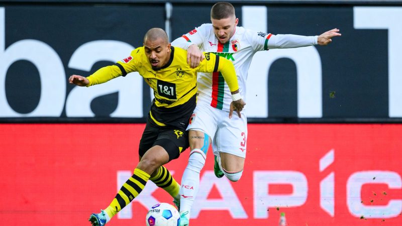 Dortmunds Donyell Malen (l) versucht den Ball vor Augsburgs Mads Pedersen (r) zu behaupten.