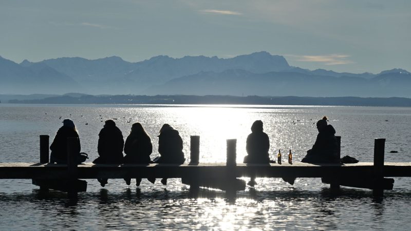 Einfach nur sein: Ausflügler sitzen auf einem Steg am Starnberger See und genießen den Blick auf die Zugspitze.