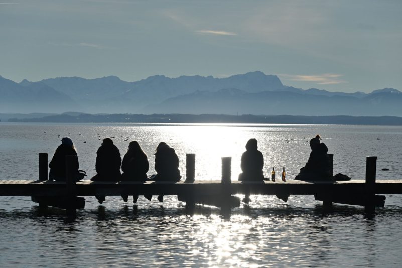 Einfach nur sein: Ausflügler sitzen auf einem Steg am Starnberger See und genießen den Blick auf die Zugspitze.