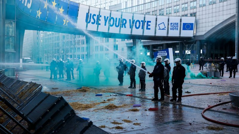 Bauernprotest in Brüssel: Beamte der Bereitschaftspolizei löschen ein Feuer, das Landwirte während einer Demonstration vor dem Europäischen Parlament gelegt haben.