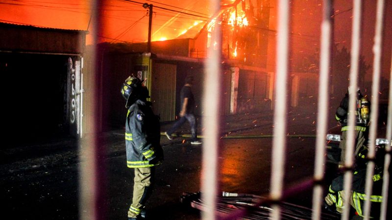 Ein Feuerwehrmann blickt nach oben, als die Flammen eines Waldbrandes auf Gebäude übergreifen.