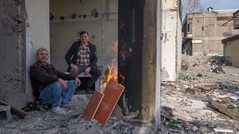 Zwei Männer wärmen sich in den Trümmern eines zerstörten Hauses in Kahramanmaras an einem Feuer. Im Zentrum der Stadt waren bei dem Beben vor einem Jahr unzählige Häuser zerstört oder beschädigt worden.