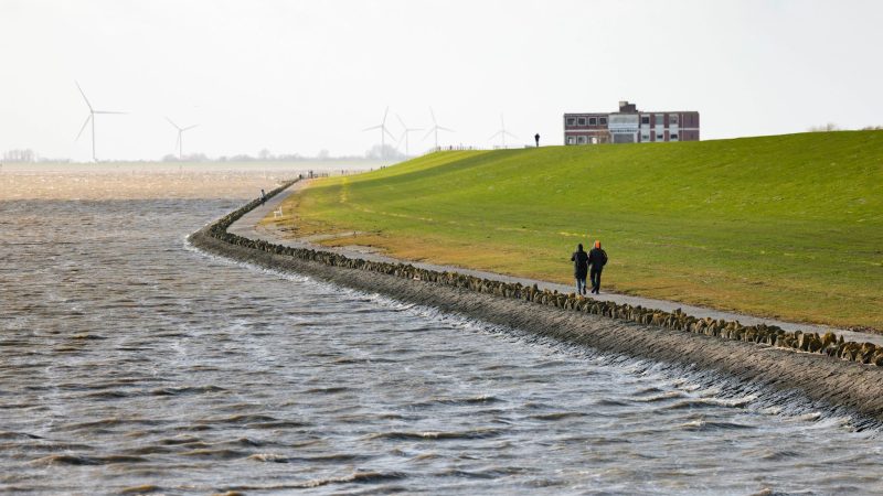 Ein Mann und eine Frau gehen an einem Deich an der Nordsee spazieren: An Niedersachsens Nordseeküste laufen die Vorbereitungen für die Saison.