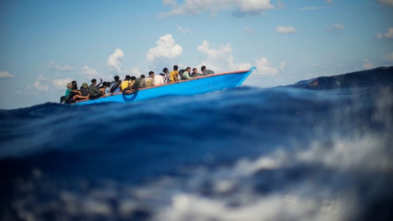 Menschen, die nach Europa wollen, sitzen in einem Holzboot im Mittelmeer. Symbolbild