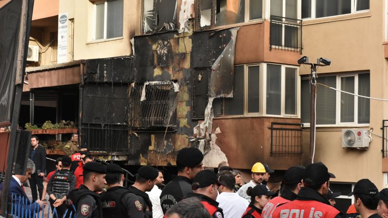 Einsatzkräfte stehen nach einem Brandausbruch vor einem teilweise verbrannten Gebäude.