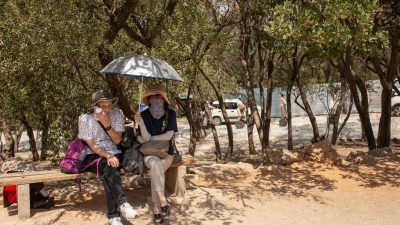 Touristen unter Bäumen am Eingang der Akropolis im Hitzesommer 2023.