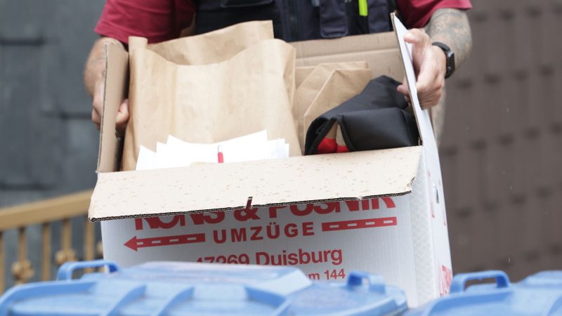 Ein Polizist trägt nach einer Wohnungsdurchsuchung einen Karton mit sichergestellte Gegenständen.